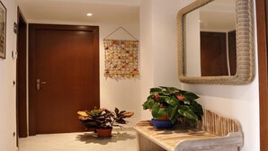 A hallway with a wooden door, a hanging fruit basket, a mirror, and two potted plants. - Cozy Apt for 4/6 persons near the sea well linked with the center of Rome (Lido di Ostia)