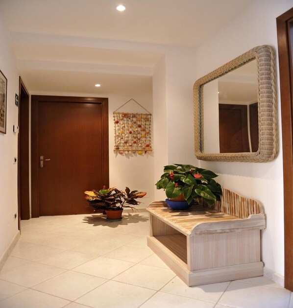 A hallway with a wooden door, a hanging fruit basket, a mirror, and two potted plants.