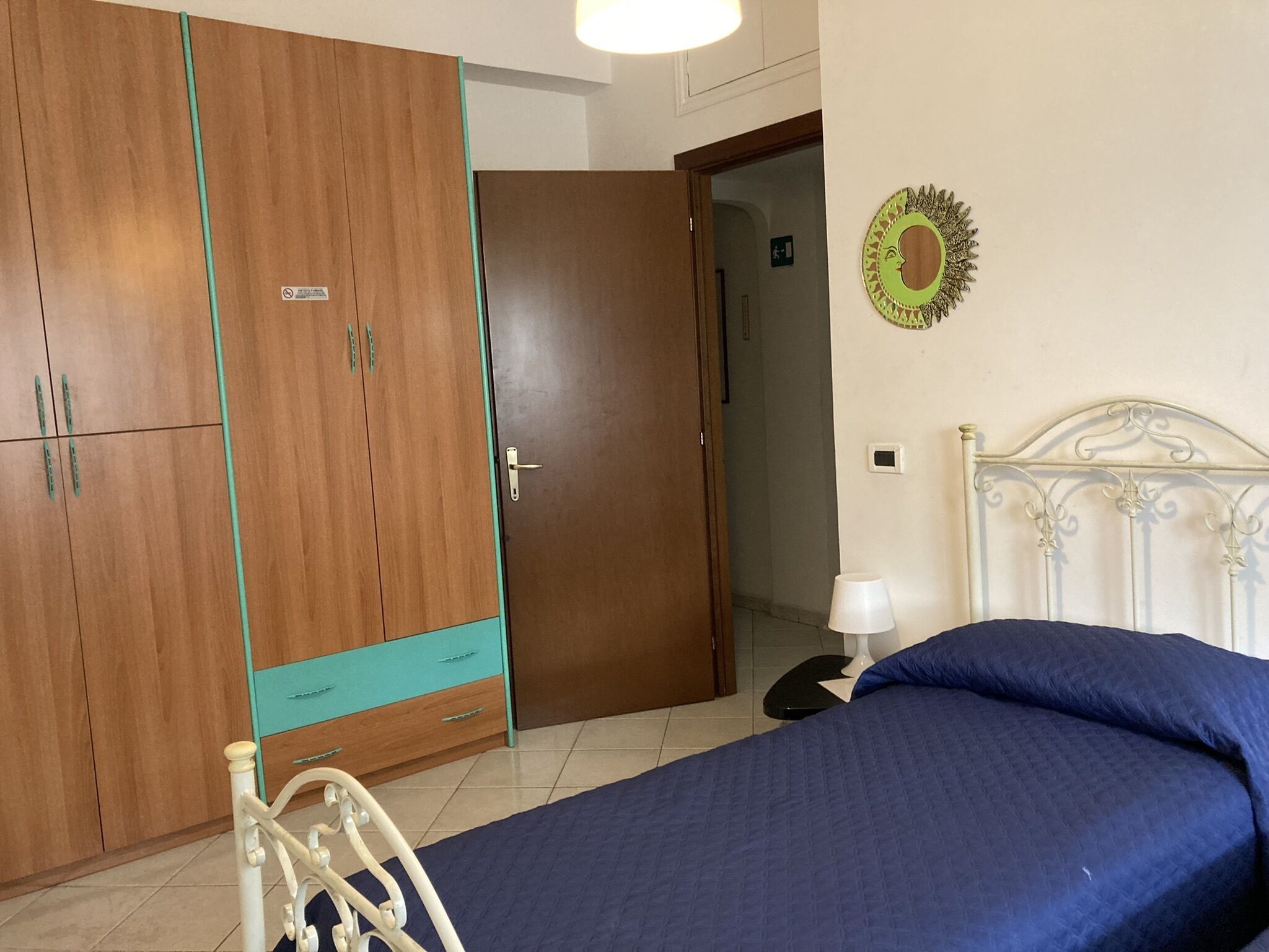 A bedroom with a bed, a wardrobe, a nightstand, a lamp, and a wall decoration.