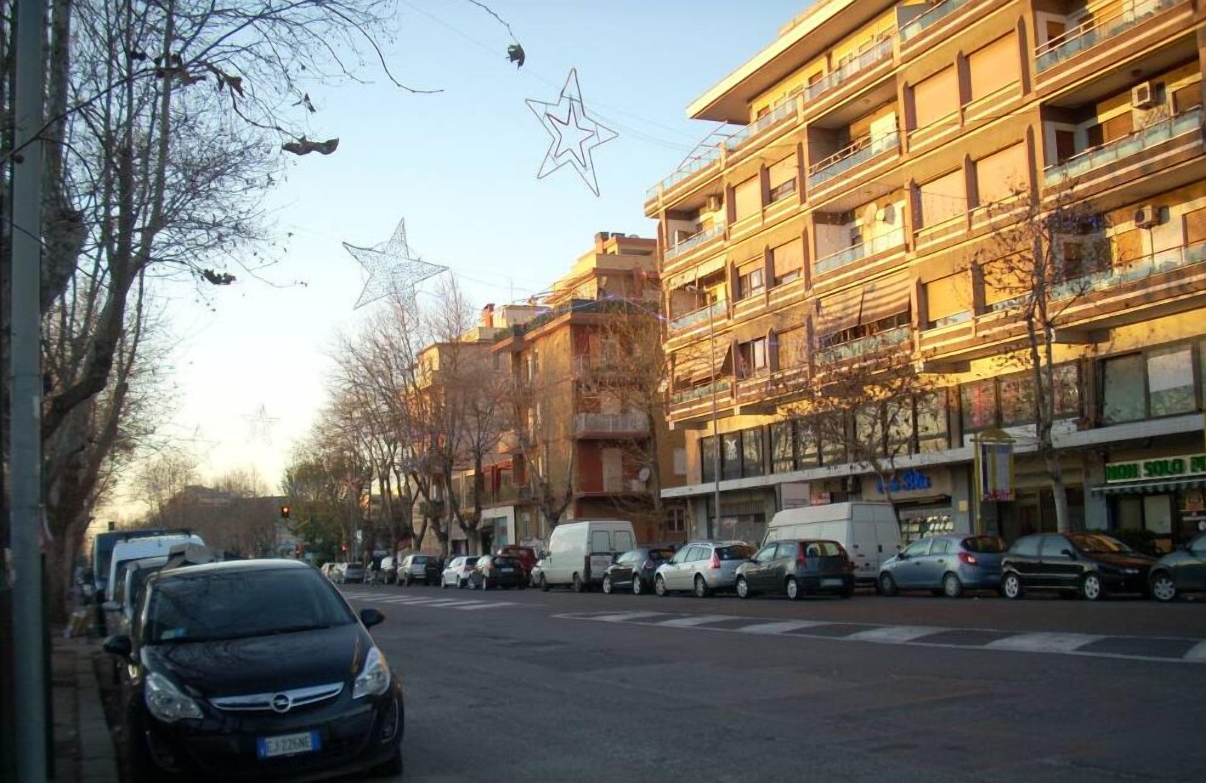 A street view with multi-story buildings, parked cars, and bare trees.