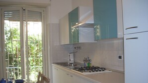 A kitchen with a gas stove, cabinets, and a window with a view of greenery. - Cozy Apt for 4/6 persons near the sea well linked with the center of Rome (Lido di Ostia)
