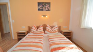 Een tweepersoonsbed met gestreepte beddengoed, een houten hoofdbord, nachtkastjes, een schilderij aan de muur en een raam met gordijnen.