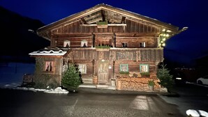 Een houten chalet met een balkon, een met sneeuw bedekt dak en een goed verlichte ingang.
