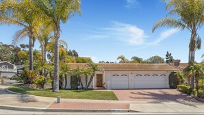 A two-story house with a garage, surrounded by palm trees and a well-maintained lawn.