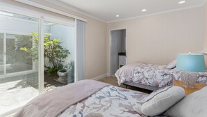 A bedroom with two beds, a large sliding glass door to a garden, and a bathroom visible through an adjacent door.