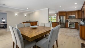 A modern kitchen with wooden cabinets, stainless steel appliances, and a dining area with a wooden table and upholstered chairs.
