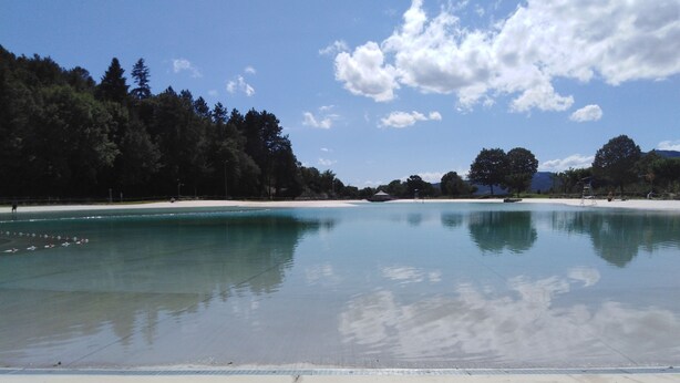 Una playa tranquila con agua cristalina, una orilla de arena y un área boscosa al fondo.