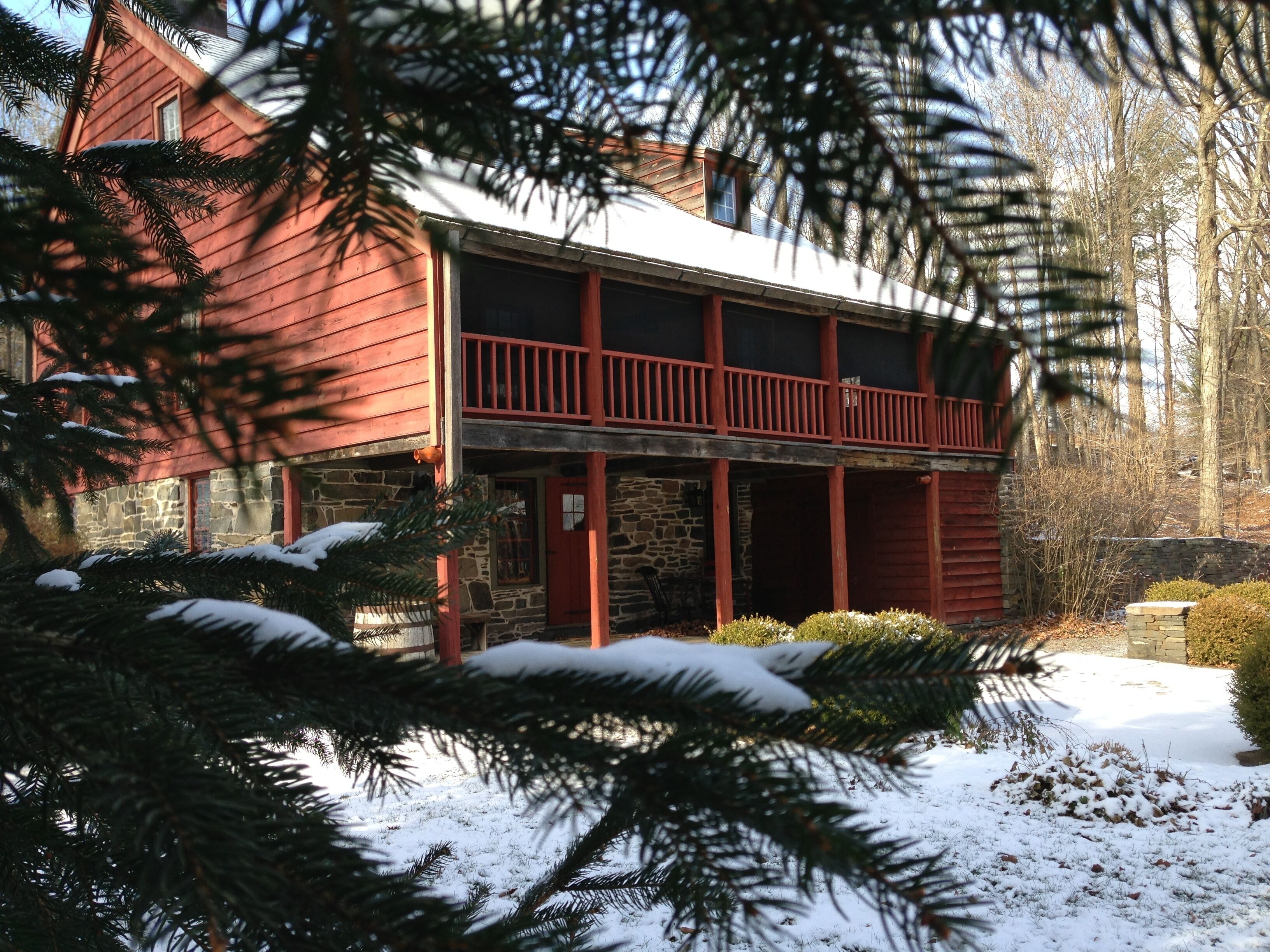 Une cabane en rondins à deux étages, avec des fondations en pierre, un balcon rouge et de la neige au sol.