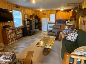 A cozy cabin interior with a wooden interior, a dining table, a sofa, and a kitchen area.