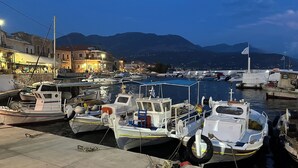 Un port de plaisance avec des bateaux amarrés, un bâtiment situé au bord de l’eau et des montagnes en arrière-plan.