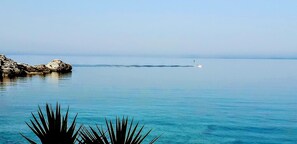 Mar tranquila con un barco a la distancia y formaciones rocosas a la izquierda.