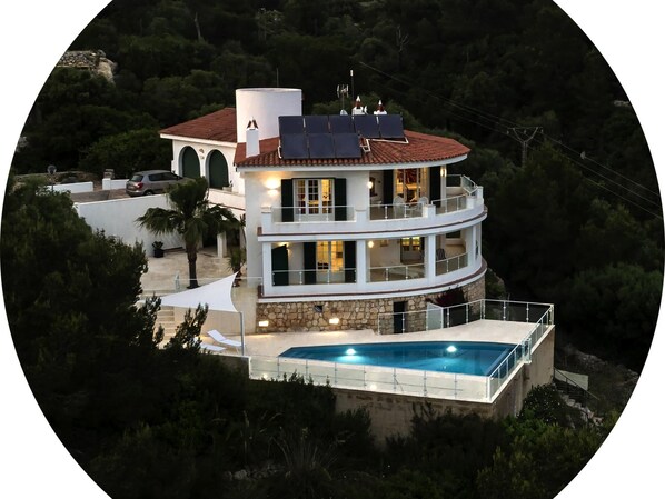 A multi-story house with a swimming pool, surrounded by greenery.