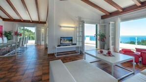 Amplia sala de estar con techo de madera, un sofá blanco, una mesa de comedor y un televisor.