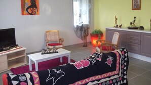 A living room with a sofa, a TV, a chair, a table, and a window with curtains. - Renovated house, close to beaches, pets allowed  (Plouégat-Guérand)