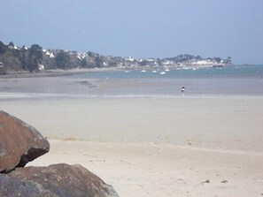 Ein Strand mit einem großen Felsen im Vordergrund, einem klaren Himmel und einer entfernten Küstenlinie mit Gebäuden.