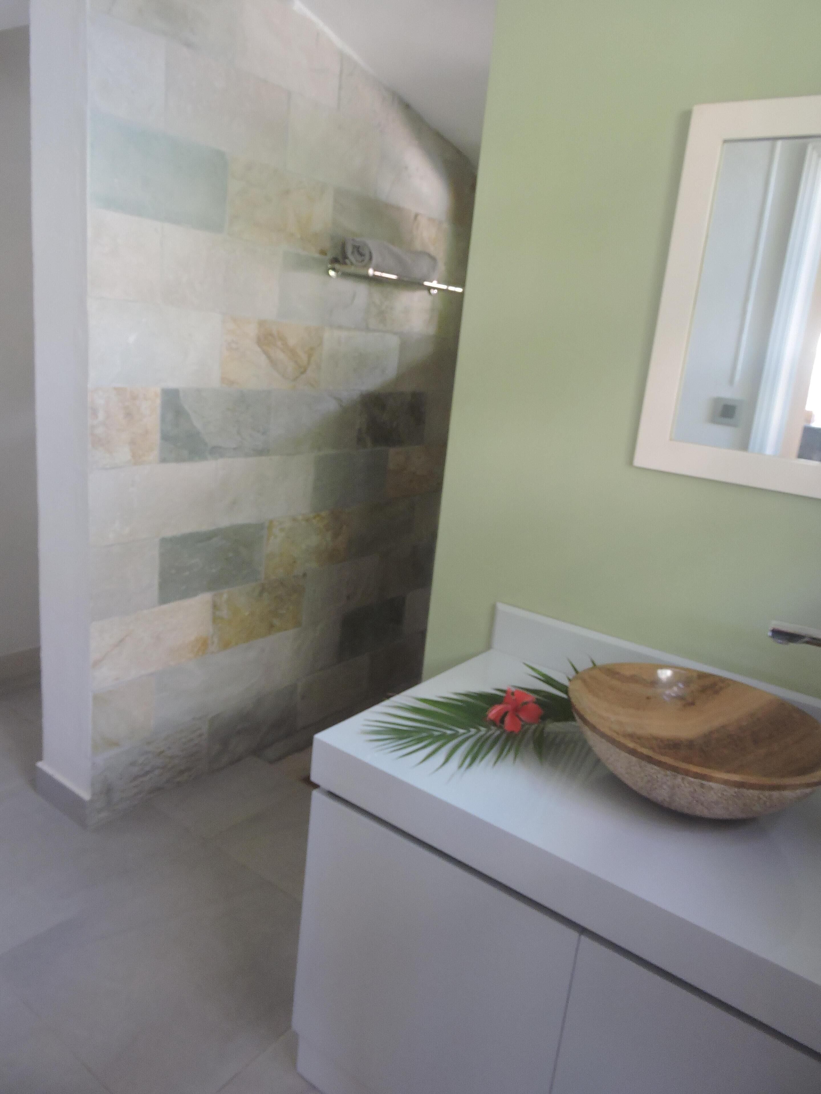 A bathroom with a stone wall, a white sink with a wooden bowl, and a mirror on the wall.