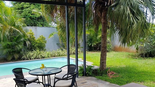 A covered patio area with a pool, a round table with chairs, and lounge chairs. - Your own villa with private pool in tropical garden.  (Grand Baie)