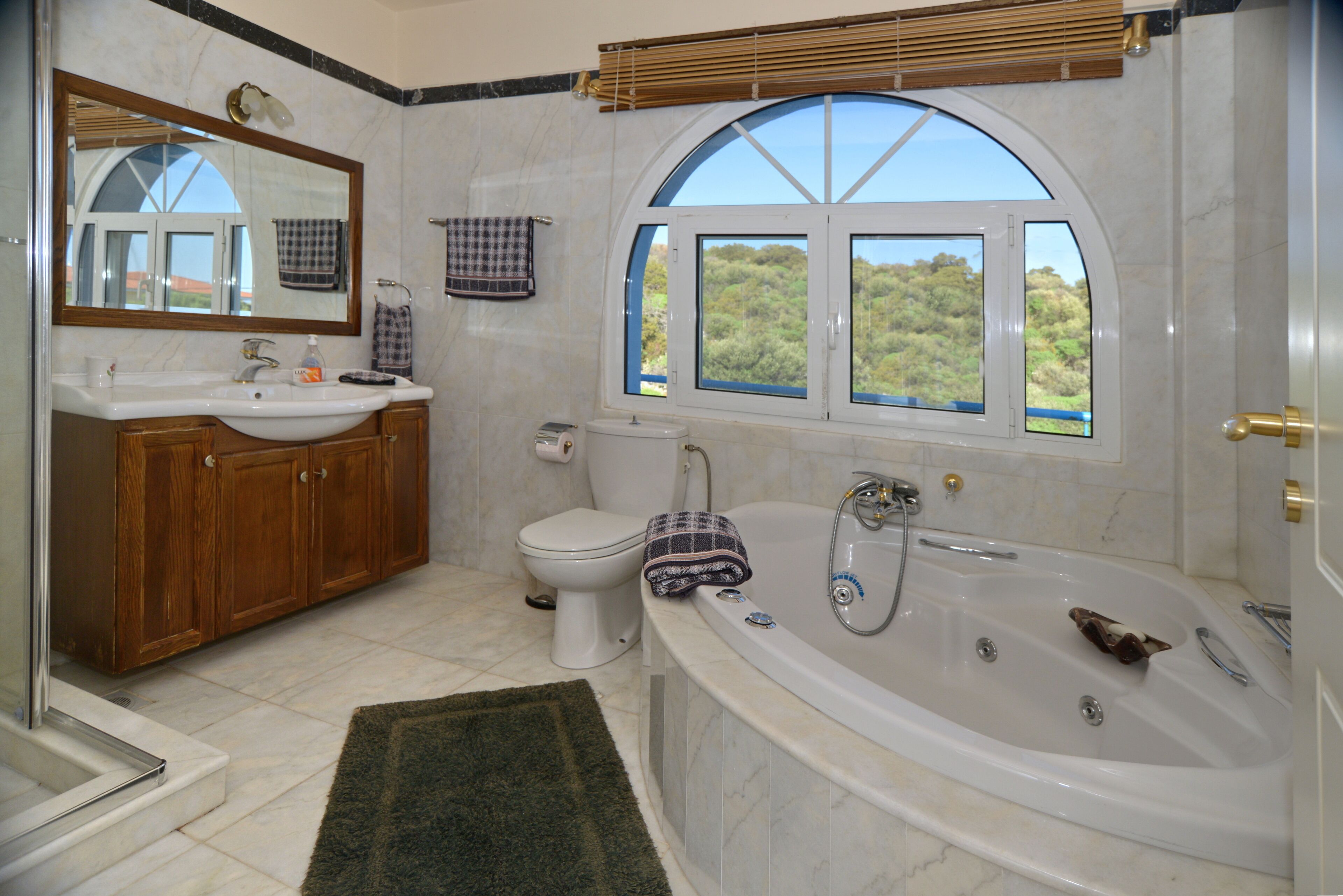 A bathroom with a large bathtub, a sink, a toilet, and a window with a view of the outdoors.