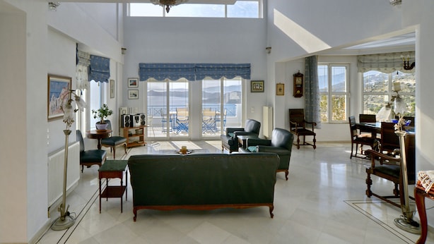 A spacious living room with a green sofa, multiple chairs, a dining table, and a view of the outdoors through large windows. - Villa Stella,  swimming pool, by the beach,  close to Athens
 (Marathon)