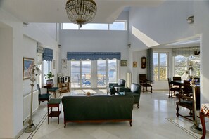 A spacious living room with a green sofa, multiple chairs, a dining table, and a view of the outdoors through large windows. - Villa Stella, swimming pool, by the beach, close to Athens
(Marathon)