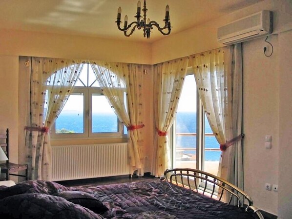 A bedroom with a bed, a radiator, a window with curtains, and a view of the sea. - Villa Stella, swimming pool, by the beach, close to Athens
(Marathon)
