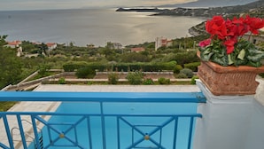 A view from a balcony overlooking a coastal area with a pool, potted plants, and distant mountains. - Villa Stella,  swimming pool, by the beach,  close to Athens
 (Marathon)