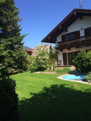Traditional chalet-style building with a sloped roof and balcony, surrounded by a well-maintained lawn and a small swimming pool.