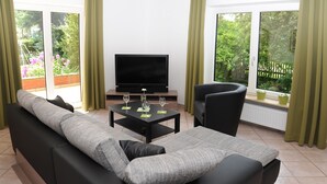 A modern living room with a sofa, a black armchair, a coffee table, and a flat-screen TV. - Attractive apartment between Munich, Tegernsee and Bad Tölz - free Wi-Fi (Sauerlach)
