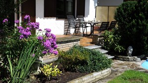 A house with a patio, outdoor seating, and a garden with purple flowers. - Attractive apartment between Munich, Tegernsee and Bad Tölz - free Wi-Fi (Sauerlach)