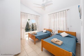 Une chambre avec deux lits, un ventilateur de plafond et un balcon avec des rideaux.