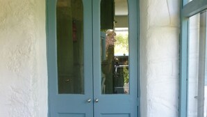 Una porta de blau clar amb dos panells de vidre, una paret blanca i una finestra amb un resguard.