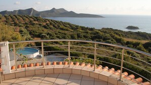 Un balcon incurvé, orné de carreaux de terre cuite, qui offre une vue sur une piscine et un paysage montagneux.