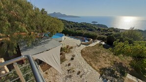 Un espace piscine doté d’une terrasse en pierre, entouré de verdure et offrant une vue panoramique sur la côte.