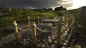 Ein steinbelagter Weg führt zu einer hölzernen Bank und einem Picknicktisch, umgeben von einem Seilabfangnetz.