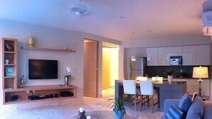 A modern living room with a flat-screen TV, wooden shelving, and a dining area with chairs and a table. - Luxury Condo, Roof Top Swimming Pool (Playa del Carmen)