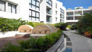 A modern hotel with a pool area, outdoor seating, and lush landscaping. - Luxury Condo, Roof Top Swimming Pool (Playa del Carmen)