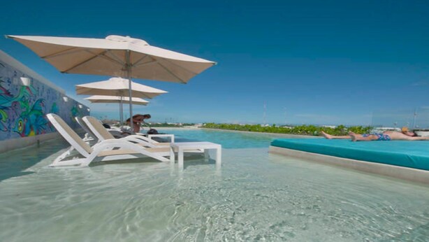 A clear pool area with lounge chairs and umbrellas, a tiled floor, and a view of the ocean. - Luxury Condo, Roof Top Swimming Pool (Playa del Carmen)