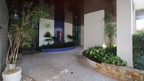 A modern building entrance with a tiled floor, potted plants, and a decorative wall.