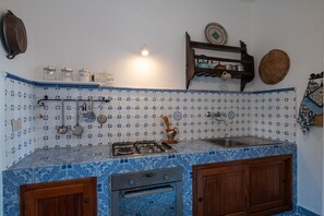 Eine Küche mit blauen, gemusterten Fliesen, einem Gasherd, einem Backofen und Holzschränken.