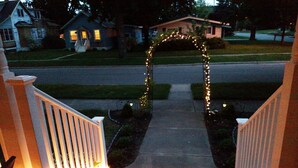 Eine Veranda mit Geländer, ein Weg, der zu einem Haus führt, und Lichterketten.