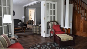Ein geräumiges Wohnzimmer mit dunklem Holzboden, einem roten Sofa, einem gemusterten Sessel und einer Holztreppe.