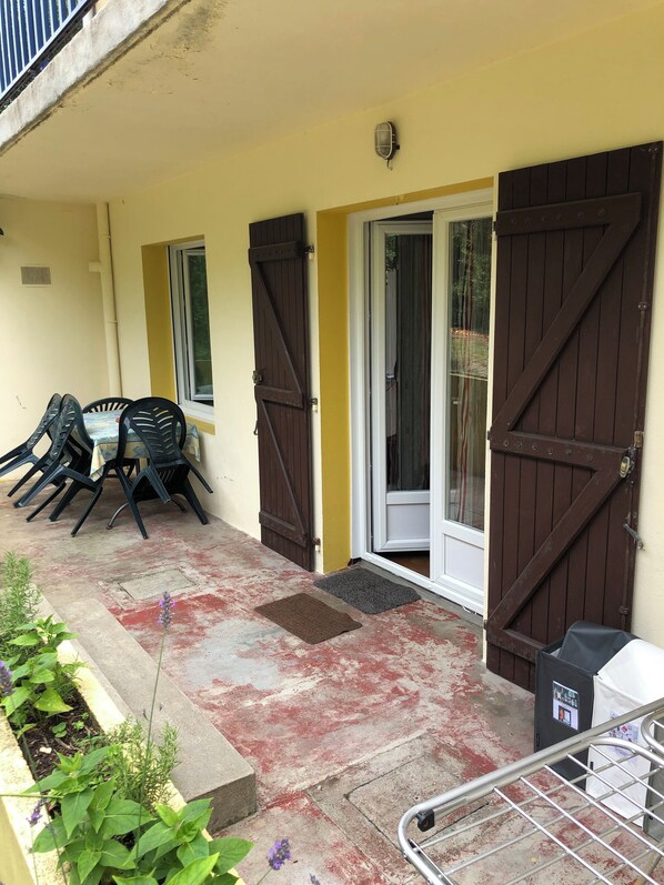A covered outdoor area with a table and chairs, a door, and a metal railing.