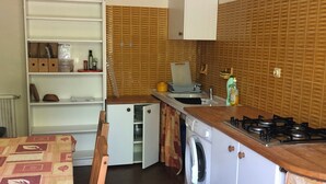 Een compacte keuken met een ingebouwde wasmachine, een klein eethoekje en een wit kastje boven de spoelbak.