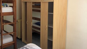 Een slaapkamer met een stapelbed, een houten garderobe met verschillende vakken, en een radiator.