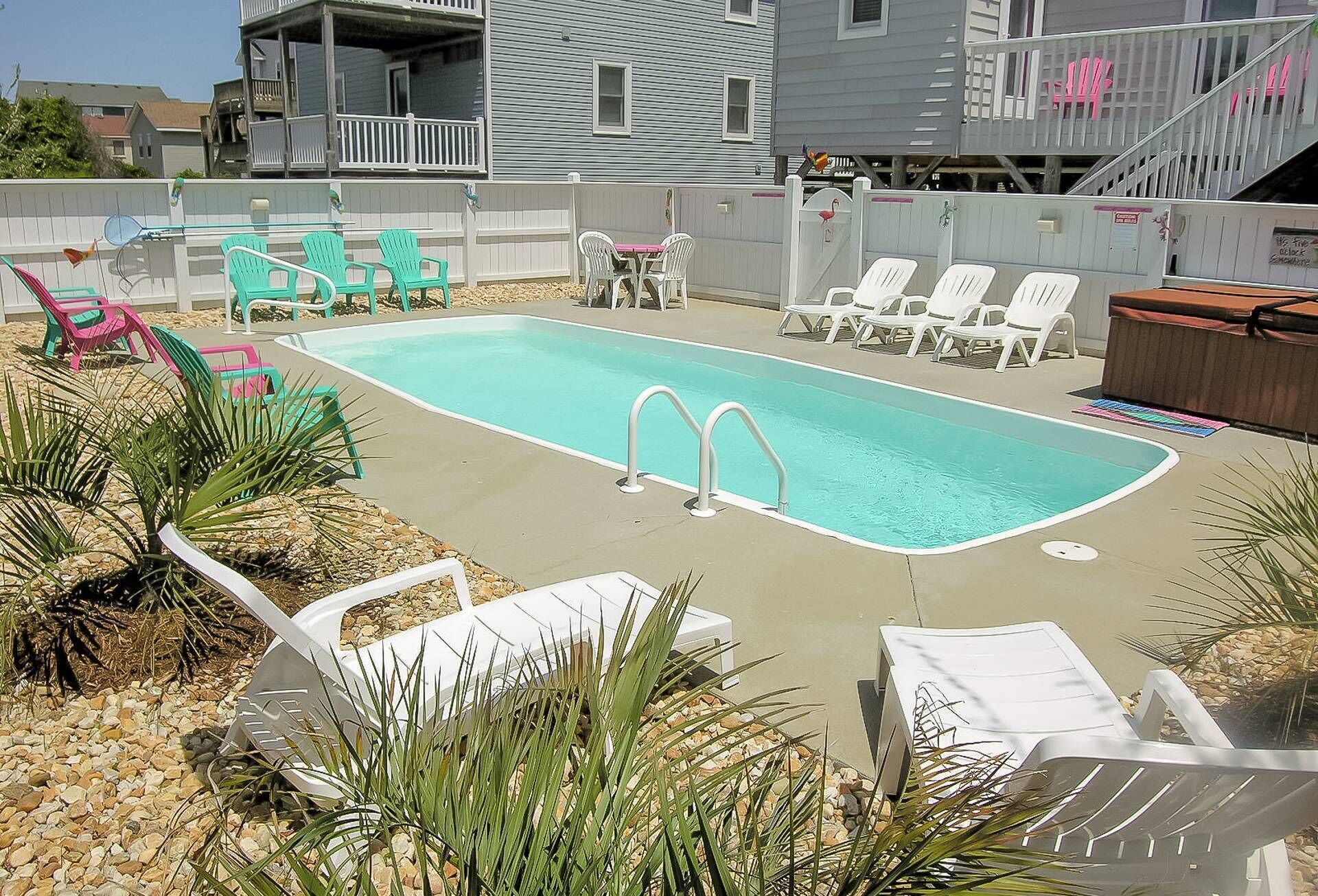 A rectangular swimming pool with two diving boards, surrounded by white lounge chairs and a few green chairs.