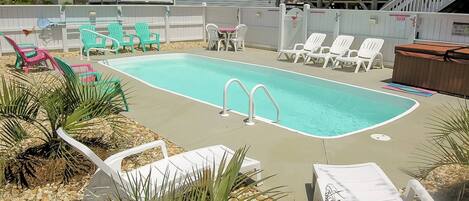 A rectangular swimming pool with two diving boards, surrounded by white lounge chairs and a few green chairs.