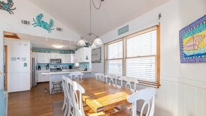A spacious kitchen with white cabinets, a wooden dining table, and a large window with blinds. - Key to Paradise - Kitty Hawk MP 4, Pool, Hot Tub, Excellent Ocean View, Easy Beach Access (Kitty Hawk)