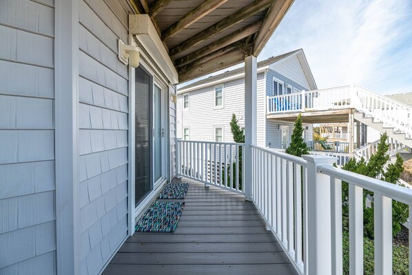A wooden deck with a white railing, leading to a covered porch area. - Key to Paradise - Kitty Hawk MP 4, Pool, Hot Tub, Excellent Ocean View, Easy Beach Access (Kitty Hawk)