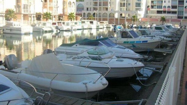 Un port esportiu amb diverses embarcacions amarrades, envoltat d'edificis amb finestres i balcons d'arc.