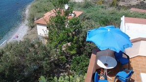 Une propriété située en bord de mer, dotée d’un patio avec une table et des chaises, un parasol bleu et une vue sur la mer.